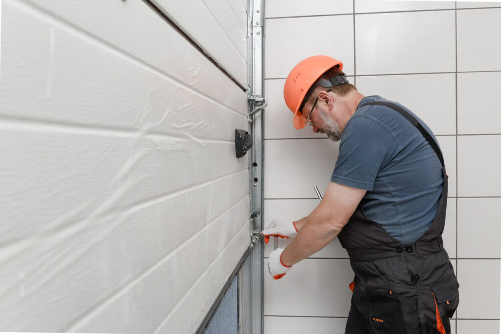 Technician in a hard hat adjusting rollers and track on a white wood-grain garage door
